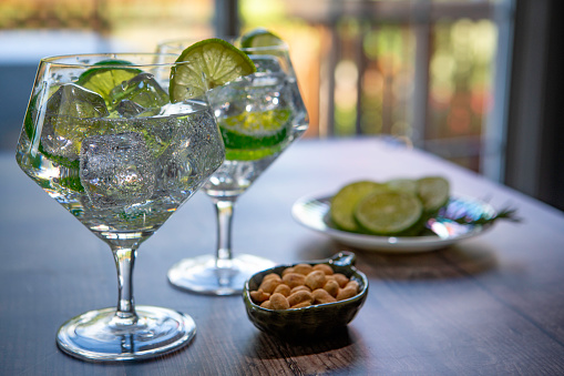 two gin and tonics on a table with lime and snacks.