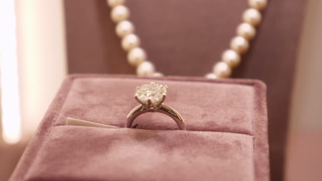 Close up of 4 carats diamond ring in brilliant cut on a display at luxury jewellery boutique. Pearl necklace on the back