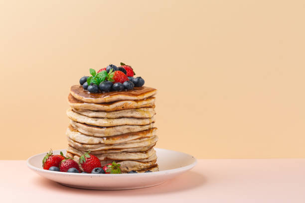 istock A stack of pancakes with honey, strawberries and blueberries. Copy space, text box. Peach and pink background. 1270100016