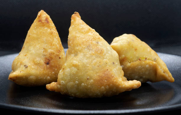 istock Three golden brown samosas on a black plate. 1270100466
