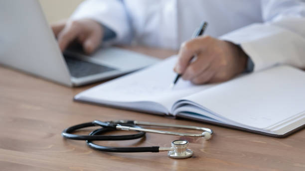 istock Close up mature doctor filling documents and using laptop 1270103996