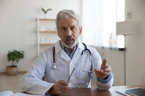 Head shot serious mature doctor wearing uniform speaking at camera