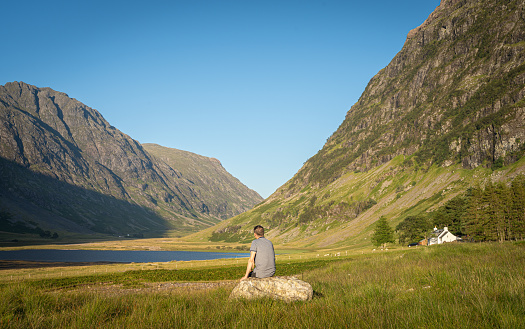 Scenic view of Loch Achtriochtan in Glen Coe, Scottish Highlands, UK. Back view of an unidentified man looking at beautiful nature and mountains during sunset