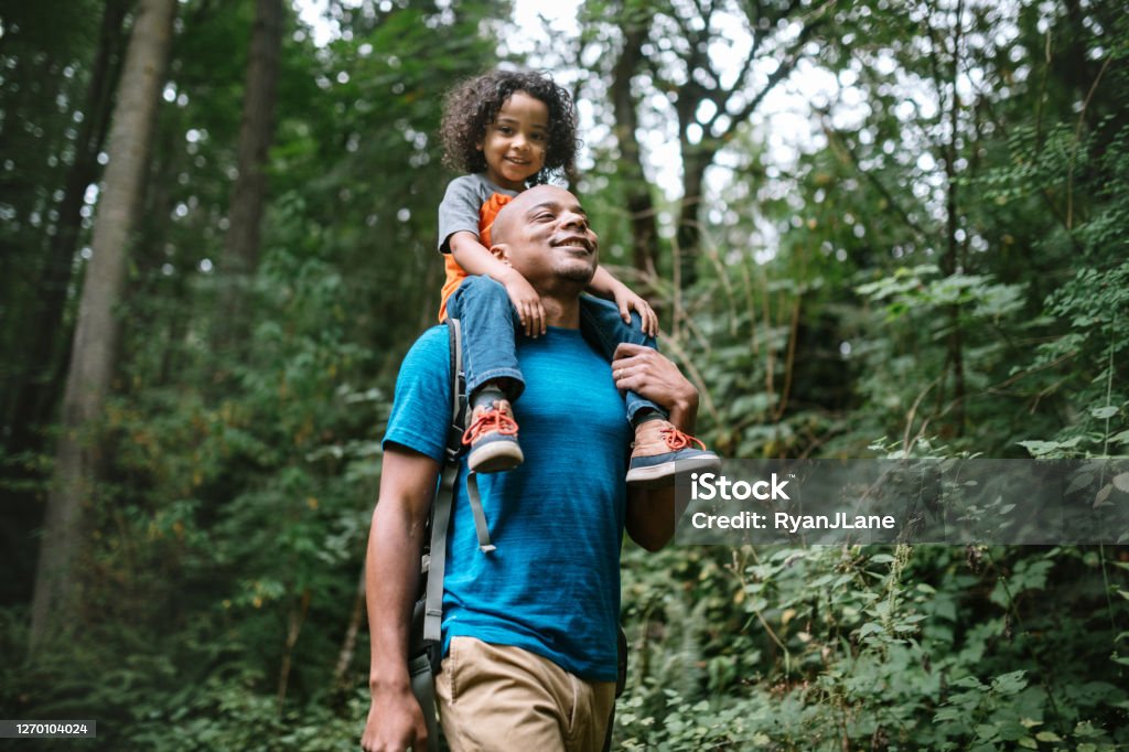 Father Carries Son On Hike Through Forest Trail in Pacific Northwest A young mixed race family spends time together outside in Washington state, enjoying the beauty of the woods in the PNW.  The dad holds his boy on his shoulders. Family Stock Photo