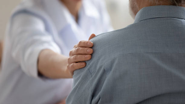 Close up caring doctor touching mature patient shoulder Close up caring doctor touching mature patient shoulder, expressing empathy and support, young woman therapist physician comforting senior aged man at meeting, medical healthcare and help general view stock pictures, royalty-free photos & images