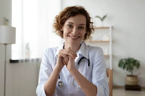 Head shot portrait smiling woman doctor wearing white uniform consulting patient online, friendly nurse physician gp looking at camera, blogger shooting video, telemedicine concept