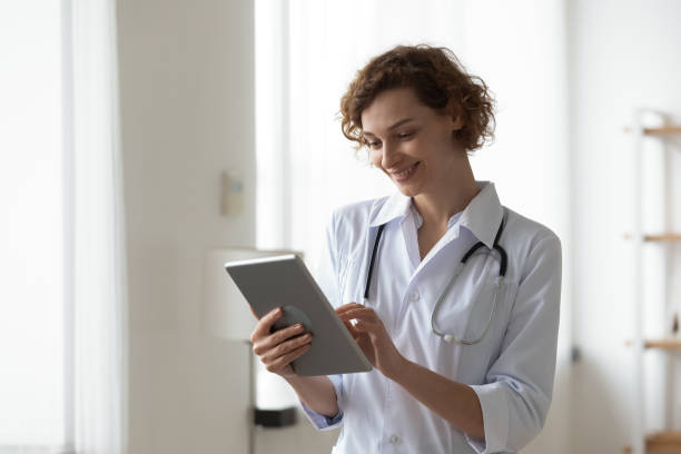 istock Smiling woman professional doctor using digital tablet, standing in office 1270104124