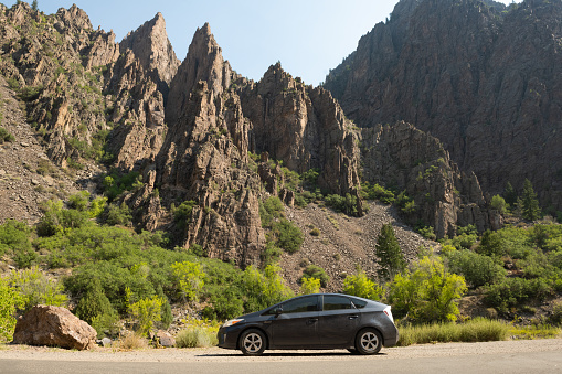 In Black Canyon of the Gunnison National Park, United States a gray Toyota Prius Hybrid car on a cross country road trip is parked along side the East Portal road and is surrounded by the rugged Colorado landscape on a summer morning.