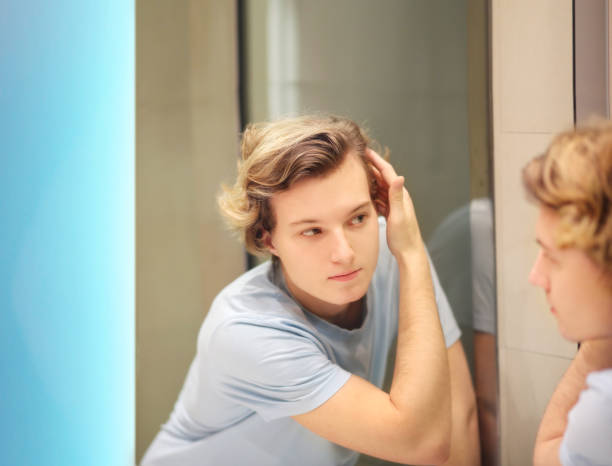 istock young man looking in the mirror,combing his hair,looking at problems on face 1270118031