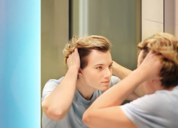 istock young man looking in the mirror,combing his hair,looking at problems on face 1270118039