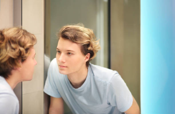 istock young man looking in the mirror,combing his hair,looking at problems on face 1270118047