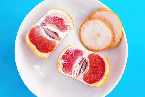 Two halves of sliced grapefruit on white plate on blue background. Diet concept, top view.