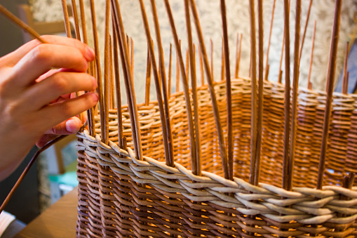 A woman weaves a basket from a paper vine. The hands of the master are shown.