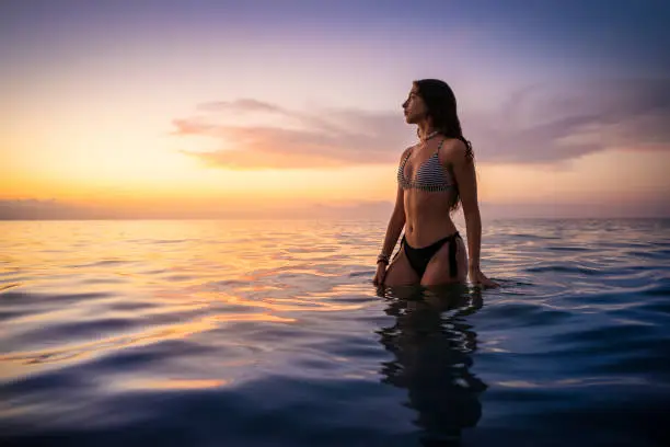 Young woman bikini girl teenager tourist on the beach looking at sunset in the ocean sea in summer vacation