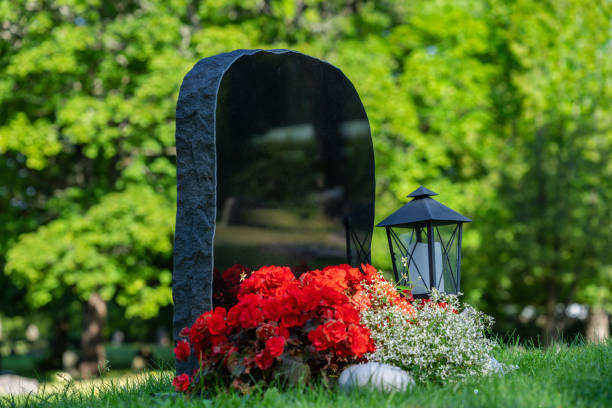 A christian grave with red flowers marked with an iron cross in the lawn.