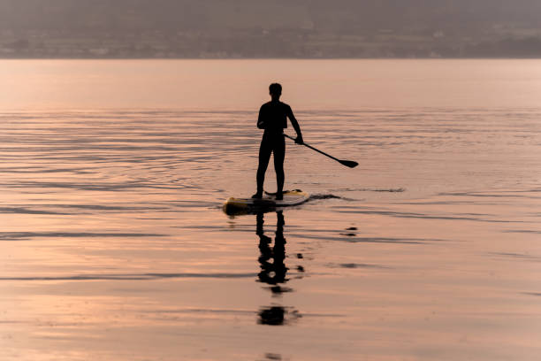 Silhouette of a young man on a paddle board at sunset stock photo