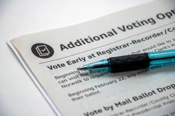 Closeup of the top corner of a booklet page entitle 'Additional Voting Options', focused on the heading 'Vote Early at Registrar' with a pen laying on top.