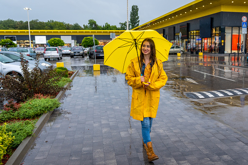 Young happy woman walking on a rainy day. She is well prepared with yellow raincoat and umbrella.