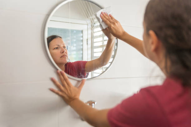 Woman cleaning a round mirror on the wall, wipping it with paper.