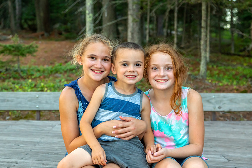 Close-up front view of three young children (two sisters and their younger brother) posing for a photo while hiking out in the woods.