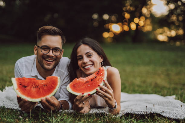 Posing for picture, green background. Portrait of two lovers, eating watermelon and smiling at camera. black man eating watermelon stock pictures, royalty-free photos & images