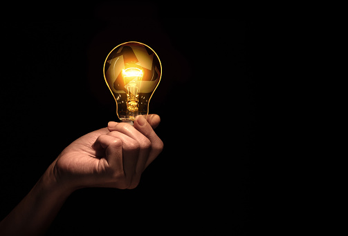 Hand holding bulb with recycle symbol inside isolate on black background.