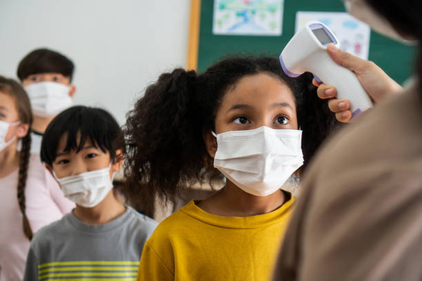 istock Group of diverse students in school building checked and scanned for temperature check. Elementary pupils are wearing a face mask and line up before entering into classroom. 1270172174