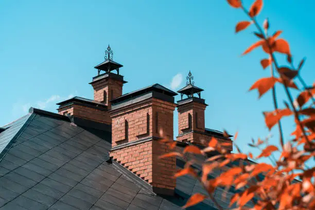 A small red brick house with a beautiful copper roof and chimneys against a clear sky.