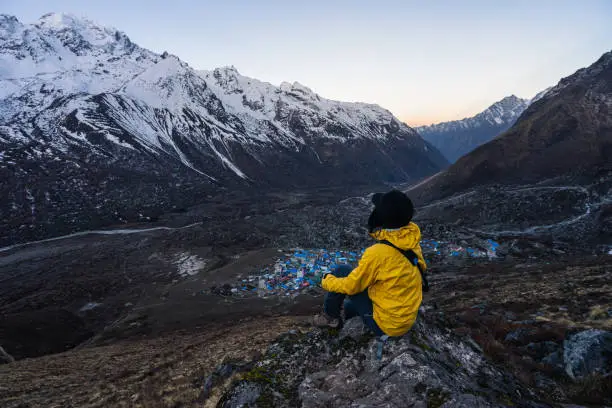 Young woman trekker sitting on rock on top of Kyanjin Ri view point in a morning sunrise, Himalaya mountains range, Nepal, Asia