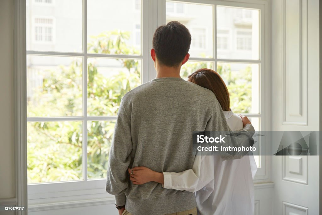 young asian couple staying at home rear view of a young asian couple looking out of window during staying at home order Couple - Relationship Stock Photo