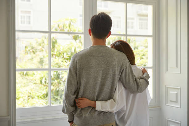 young asian couple staying at home rear view of a young asian couple looking out of window during staying at home order worried man standing stock pictures, royalty-free photos & images