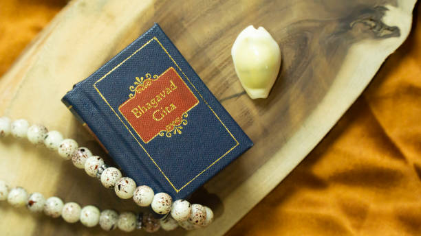 Hindu Holy book 'Bhagvad Gita' kept on a wooden base with other spiritual props Hindu holy book and cowrie shell on a wooden surface with golden satin cloth holy book stock pictures, royalty-free photos & images