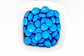 Group of small blue coated chocolate candies similar to m&ms in a squared bowl isolated on white background, top view