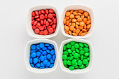 Four squared bowls with small red, yellow, blue, green and orange coated chocolate candies similar to m&ms in a squared bowl isolated on white background, top view