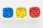 Three squared bowls with small red, yellow and blue coated chocolate candies similar to m&ms in a squared bowl isolated on white background, top view
