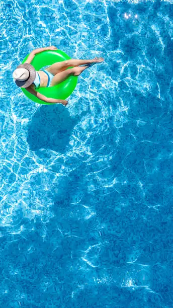 Photo of Active young girl in swimming pool aerial top view from above, child relaxes and swims on inflatable ring donut and has fun in water on family vacation, tropical holiday resort