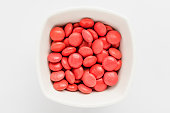 Group of small red coated chocolate candies similar to m&ms in a squared bowl isolated on white background, top view