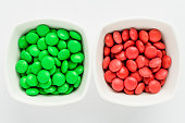 Two squared bowls with small green and red coated chocolate candies similar to m&ms in a squared bowl isolated on white background, top view