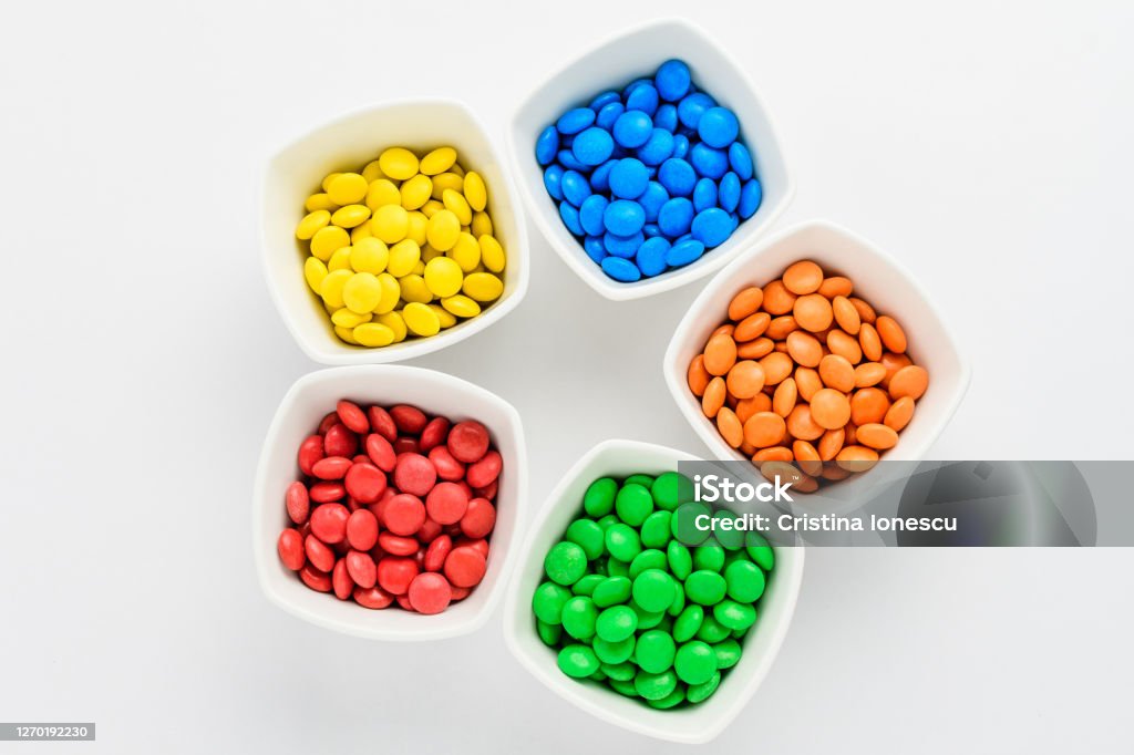 Five squared bowls with small red, yellow, blue, green and orange coated chocolate candies similar to m&ms in a squared bowl isolated on white background, top view Candy Stock Photo