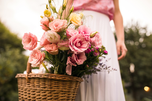 Low angle view of unrecognizable woman carrying a traditional wicker basket with pink flowers she picked up from her personal garden.