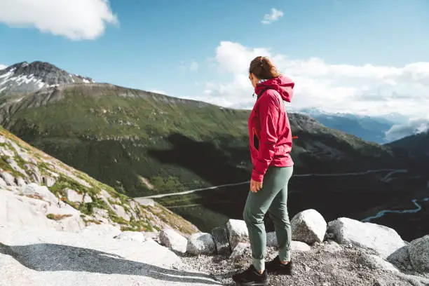 Woman traveler standing at a view point at Furka pass, enjoying the view over the mountains.