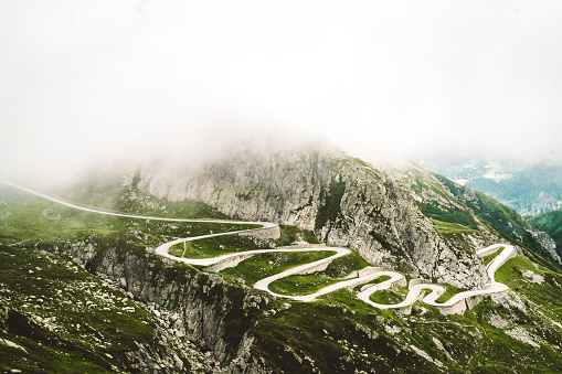 Clouds gathering over the mountains above St. Gotthard pass in Switzerland Alps. Curvy road up the mountain with no cars.