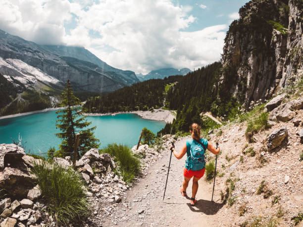 Woman hiker walking down to Lake Oeschinensee Woman hiking in the mountains by the Oeschinen lake in Berner Oberland region in central Switzerland.  Hiker hiking in Swiss alps in the summer. lake oeschinensee stock pictures, royalty-free photos & images