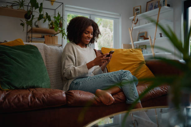 istock Happy young african woman using mobile phone while sitting a couch at home 1270222966