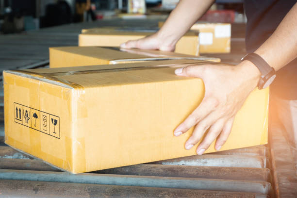 istock Close-up cardboard boxes on conveyor belt. Worker sorting parcel box in distribution warehouse. 1270224754
