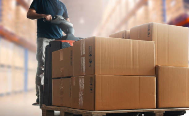 istock Shipment boxes, Cargo warehouse. Warehouse worker driving electric forklift pallet jack unloading pallet goods. 1270224755