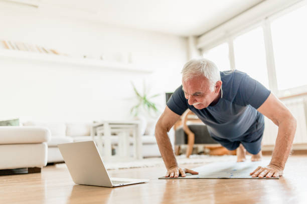 exercice actif à la maison d’homme aîné avec l’entraîneur en ligne - living room learning healthy lifestyle one person photos et images de collection