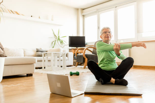 mujer senior activa en casa haciendo ejercicio con entrenador en línea - estirándose fotos fotografías e imágenes de stock