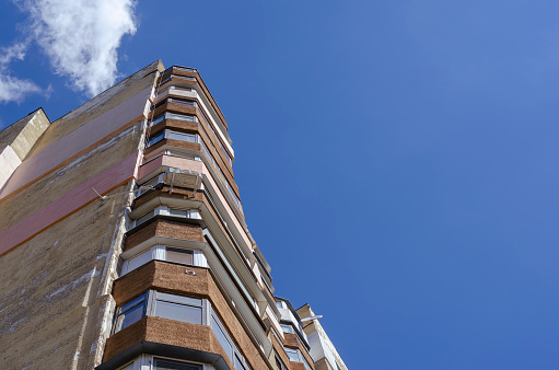 High building of an apartment building against a blue sky with clouds. The facade of an earthquake-resistant skyscraper with partially insulated external walls. Cityscape