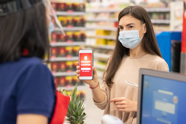 Woman Using Disount Coupon Modern woman wearing mask on face using digital discount coupon on her smartphone in supermarket coupon photos stock pictures, royalty-free photos & images